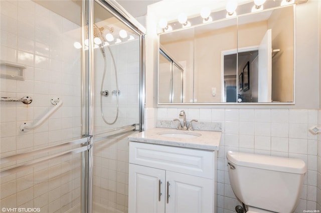 bathroom with a shower with door, vanity, tile walls, and toilet