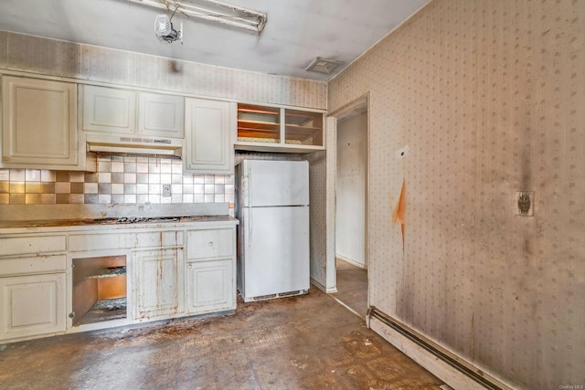 kitchen with decorative backsplash, cream cabinets, white fridge, and stainless steel gas cooktop