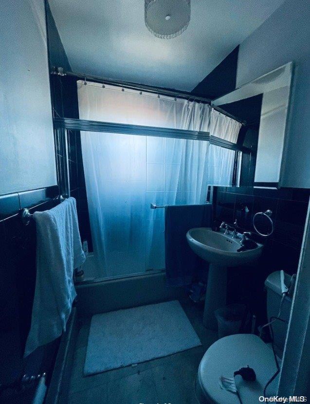 bathroom with curtained shower, sink, tile walls, and toilet