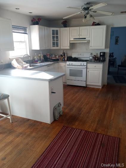 kitchen featuring dark wood-type flooring, kitchen peninsula, ceiling fan, white cabinetry, and white range with gas cooktop