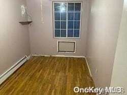 empty room with dark wood-type flooring and a baseboard heating unit