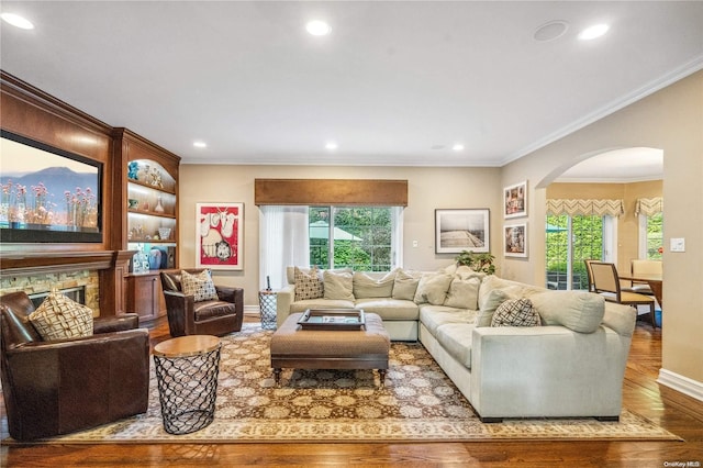 living room with a stone fireplace, crown molding, and wood-type flooring