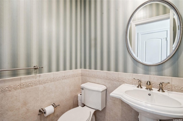 bathroom with toilet, sink, and tile walls