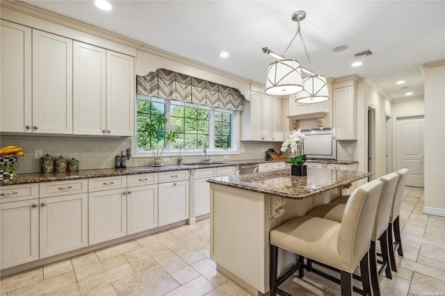 kitchen featuring backsplash, ornamental molding, dark stone counters, decorative light fixtures, and a kitchen island