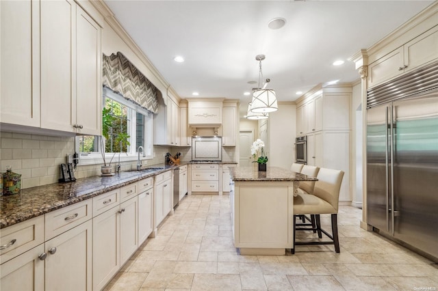 kitchen featuring pendant lighting, dark stone counters, sink, appliances with stainless steel finishes, and a kitchen island