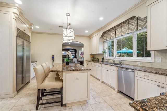 kitchen featuring dark stone countertops, decorative light fixtures, decorative backsplash, a kitchen island, and appliances with stainless steel finishes