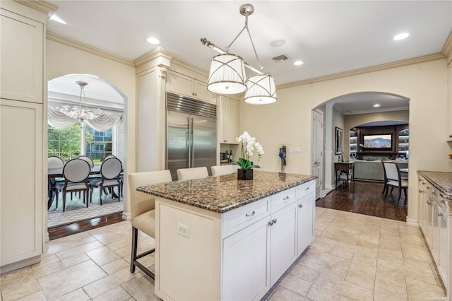 kitchen with dark stone counters, built in fridge, a kitchen breakfast bar, light hardwood / wood-style floors, and a kitchen island