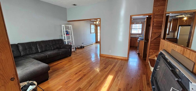 living room with ceiling fan, a high ceiling, a baseboard heating unit, and light wood-type flooring