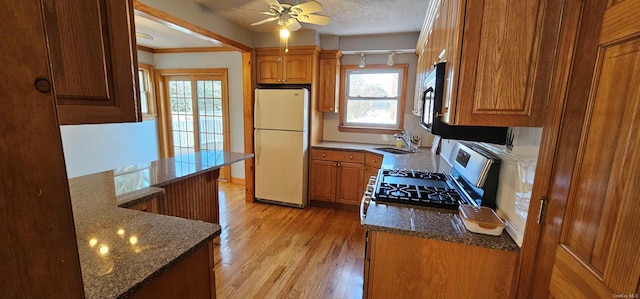 kitchen featuring light wood-type flooring, a textured ceiling, sink, white refrigerator, and stainless steel range oven