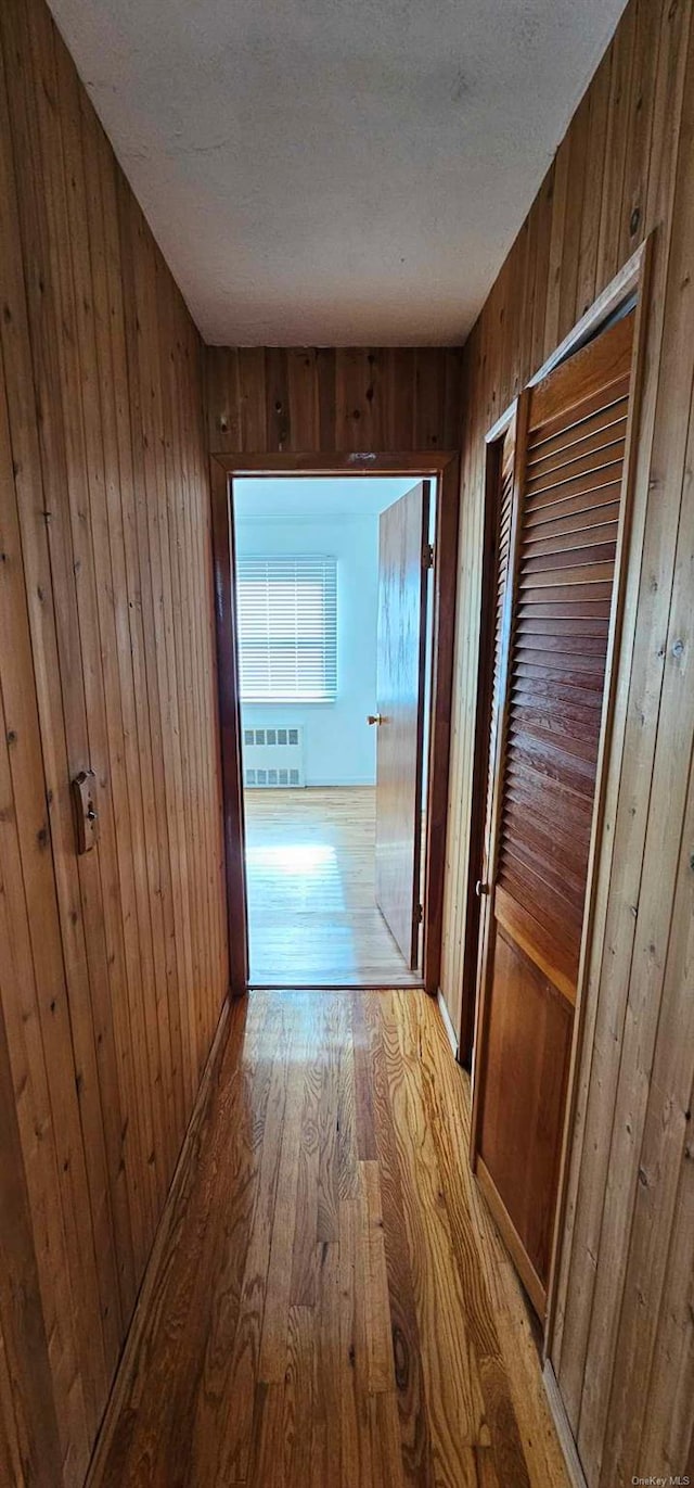 corridor with wood walls, a textured ceiling, and light wood-type flooring