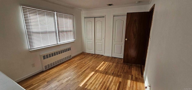 unfurnished bedroom featuring crown molding, radiator heating unit, two closets, and light wood-type flooring