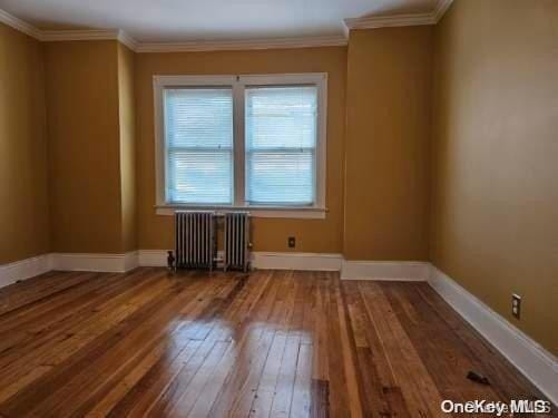 unfurnished room featuring wood-type flooring, radiator heating unit, and crown molding