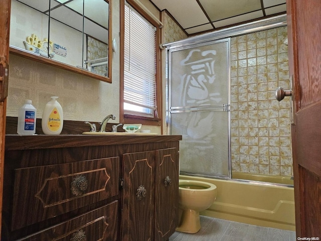 full bathroom with a drop ceiling, vanity, enclosed tub / shower combo, and toilet