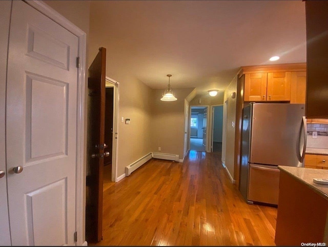 kitchen featuring stainless steel refrigerator, a baseboard heating unit, pendant lighting, light hardwood / wood-style floors, and light brown cabinetry