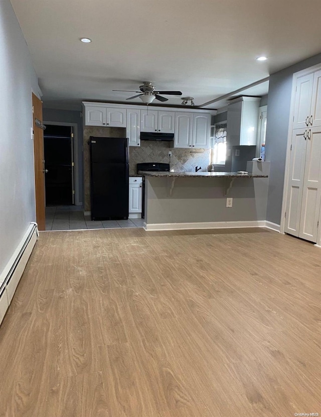 kitchen with black fridge, kitchen peninsula, dark stone countertops, light hardwood / wood-style floors, and white cabinets