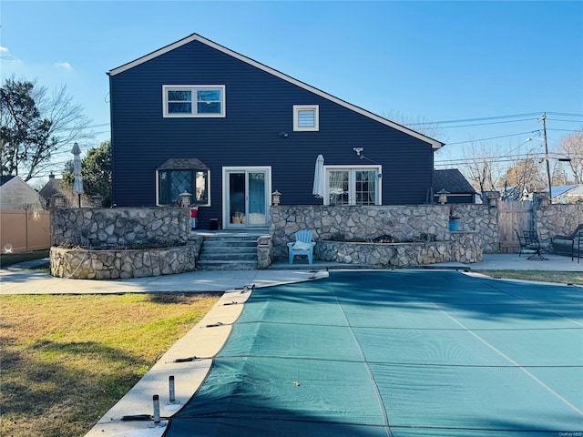 rear view of house with a covered pool, a patio, and a lawn