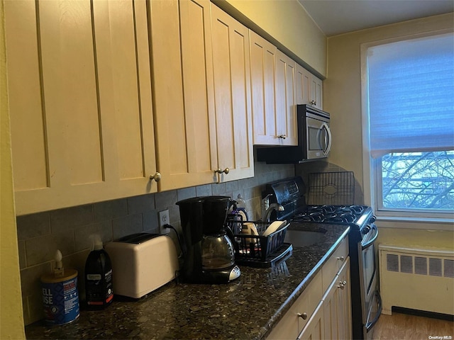 kitchen featuring radiator, dark stone counters, decorative backsplash, light wood-type flooring, and appliances with stainless steel finishes