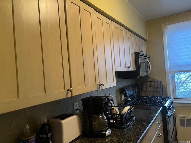 kitchen featuring dark stone countertops, radiator heating unit, appliances with stainless steel finishes, and tasteful backsplash