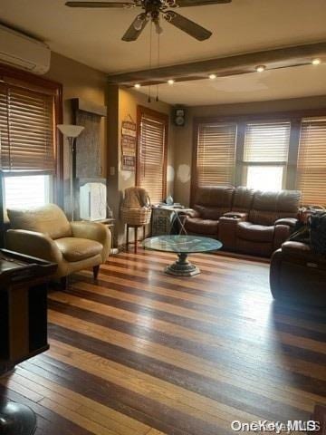 living room with ceiling fan, a wall mounted AC, dark hardwood / wood-style flooring, and beamed ceiling