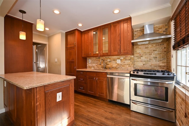 kitchen featuring light stone counters, pendant lighting, wall chimney range hood, appliances with stainless steel finishes, and sink