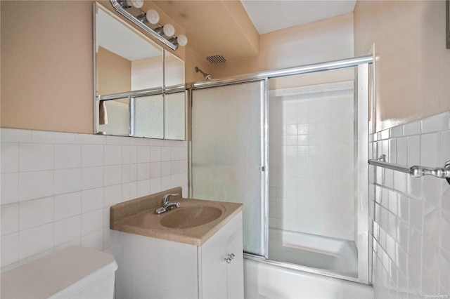 full bathroom featuring combined bath / shower with glass door, vanity, toilet, and tile walls