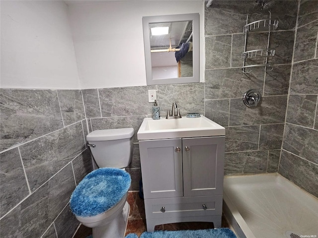 bathroom featuring tiled shower, vanity, toilet, and tile walls