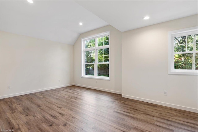 empty room featuring a healthy amount of sunlight, hardwood / wood-style flooring, and lofted ceiling