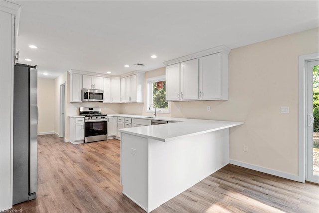 kitchen with white cabinets, appliances with stainless steel finishes, kitchen peninsula, and light hardwood / wood-style floors