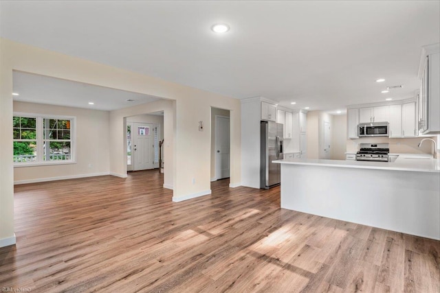 kitchen with sink, kitchen peninsula, appliances with stainless steel finishes, white cabinets, and light wood-type flooring