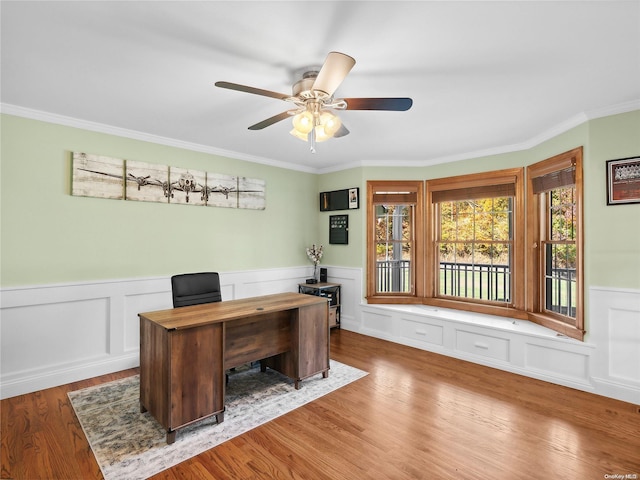 office with a decorative wall, a wainscoted wall, wood finished floors, ornamental molding, and ceiling fan