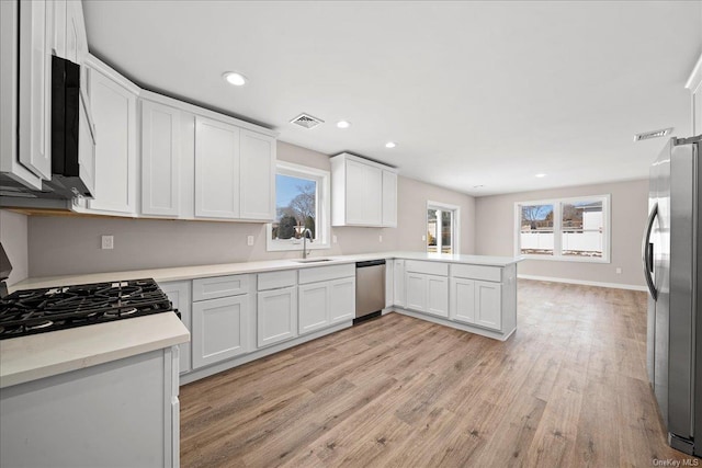 kitchen featuring light hardwood / wood-style floors, kitchen peninsula, white cabinets, and appliances with stainless steel finishes