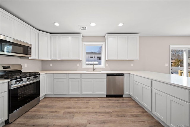 kitchen with white cabinetry, appliances with stainless steel finishes, kitchen peninsula, and plenty of natural light