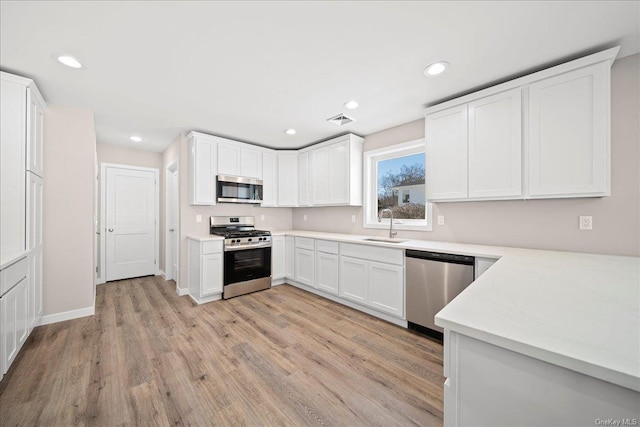 kitchen with stainless steel appliances, white cabinetry, sink, and light wood-type flooring