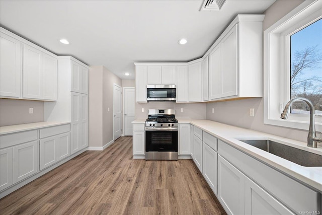 kitchen with white cabinetry, sink, stainless steel appliances, and light hardwood / wood-style floors