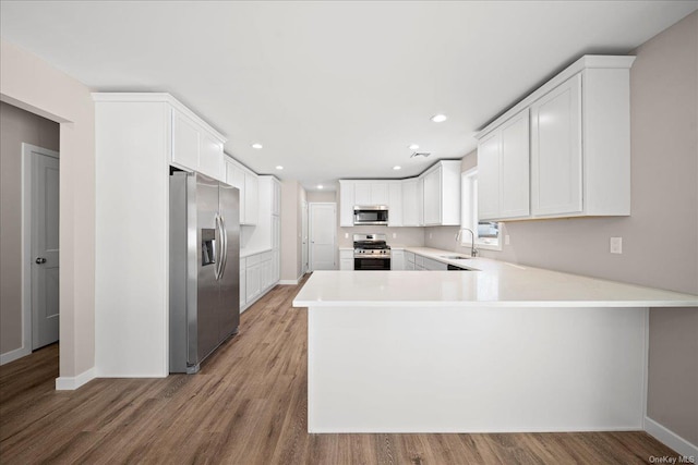 kitchen with wood-type flooring, kitchen peninsula, white cabinets, and appliances with stainless steel finishes