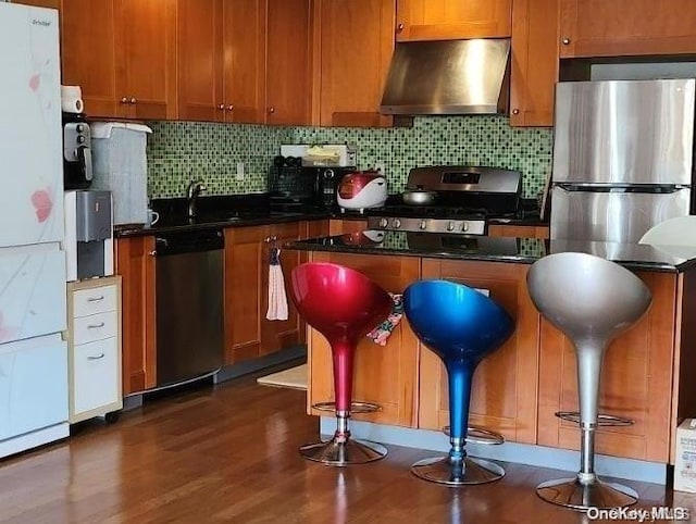 kitchen with appliances with stainless steel finishes, backsplash, dark wood-type flooring, sink, and wall chimney range hood