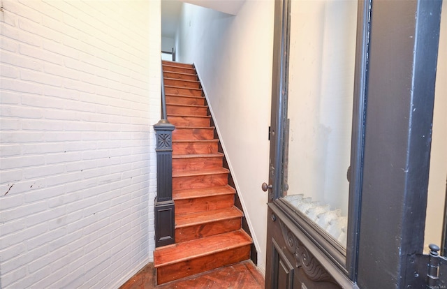 stairway with baseboards and brick wall