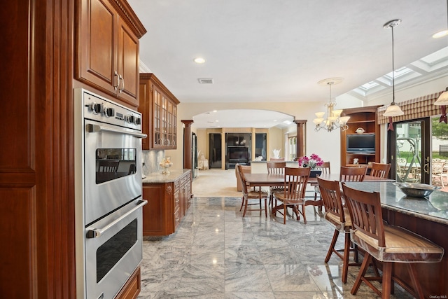 kitchen featuring double oven, arched walkways, ornate columns, visible vents, and brown cabinets