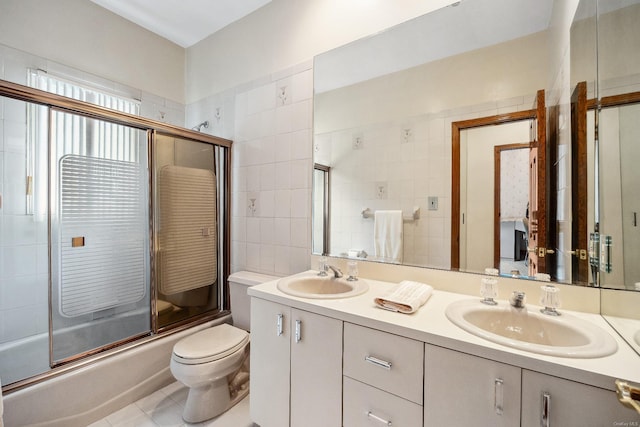 bathroom with toilet, double vanity, a sink, and bath / shower combo with glass door