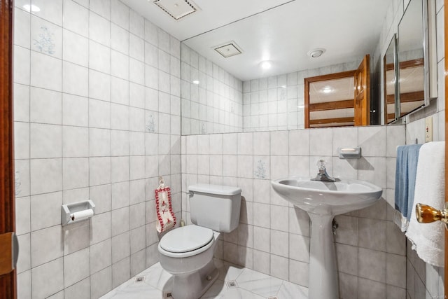 half bath with visible vents, tile walls, a sink, and toilet