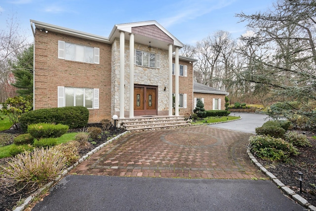 neoclassical home featuring brick siding, french doors, stone siding, and driveway