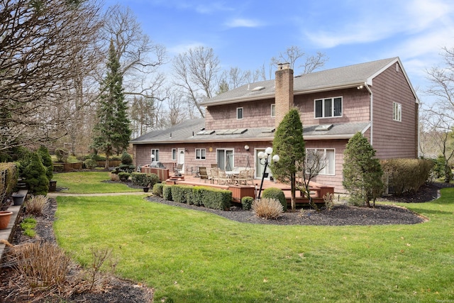 back of house featuring a yard, a wooden deck, a shingled roof, and a chimney