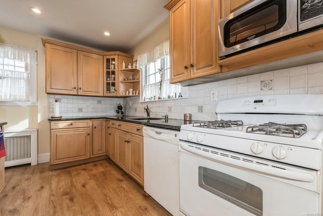 kitchen with white appliances, dark stone countertops, tasteful backsplash, sink, and light hardwood / wood-style flooring