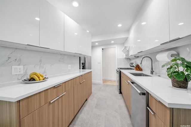 kitchen with stainless steel appliances, a sink, white cabinetry, light countertops, and modern cabinets