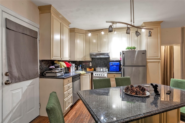 kitchen featuring appliances with stainless steel finishes, light wood-type flooring, tasteful backsplash, dark stone countertops, and hanging light fixtures