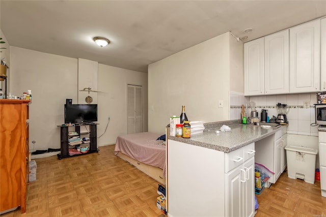 kitchen with white cabinets, decorative backsplash, sink, and light parquet flooring