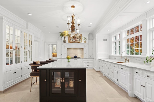 kitchen featuring white cabinetry, a center island, sink, hanging light fixtures, and light stone counters