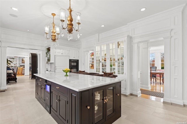 kitchen with decorative columns, ornamental molding, an inviting chandelier, a center island, and hanging light fixtures