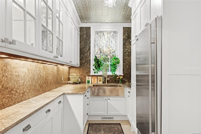 kitchen featuring white cabinetry, high end fridge, crown molding, and sink