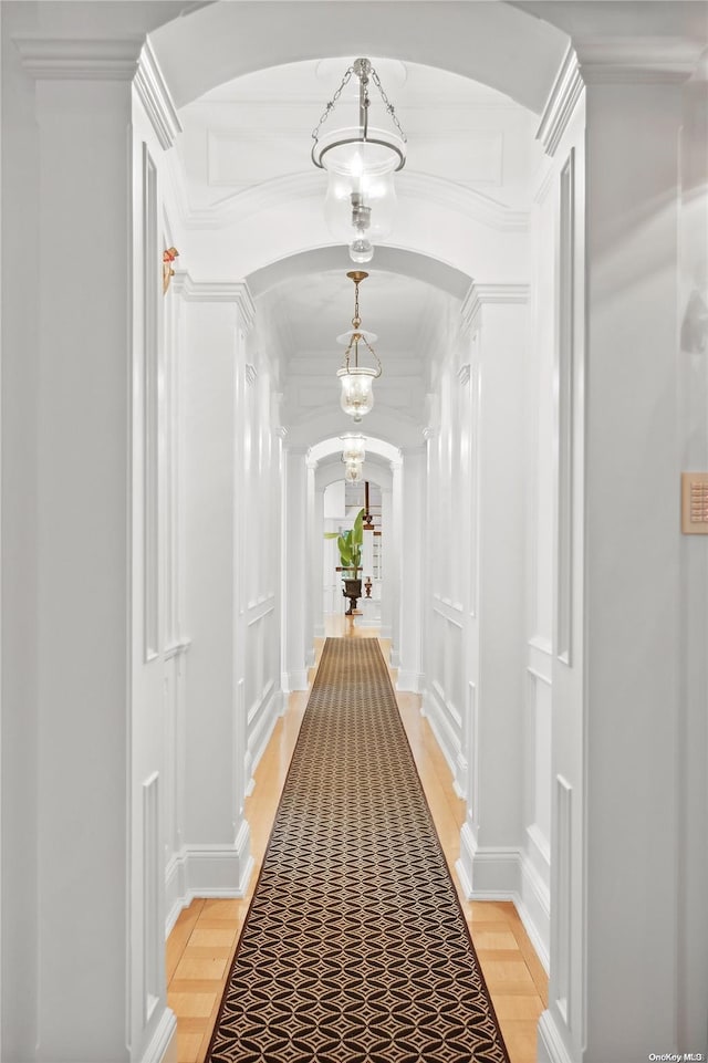 corridor with ornate columns, crown molding, an inviting chandelier, and light wood-type flooring